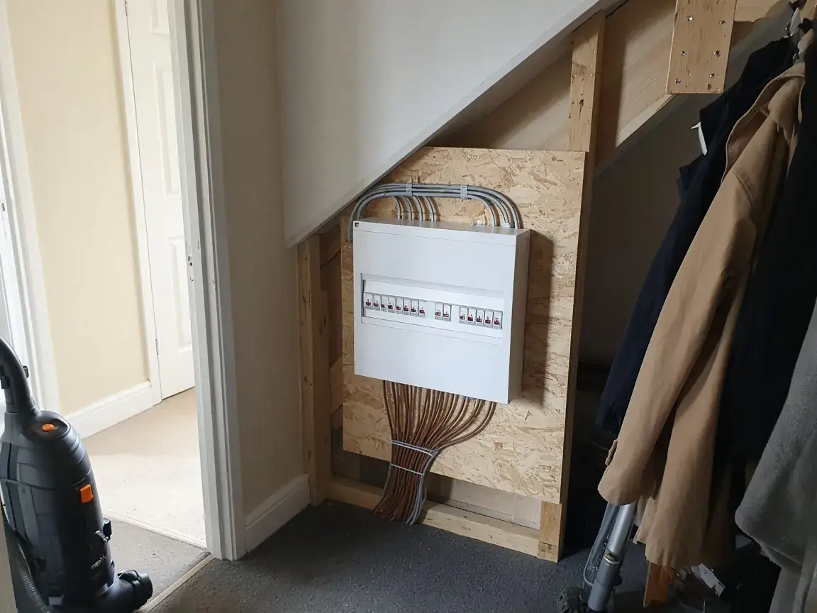 A newly fitted white consumer unit on a board under the stairs